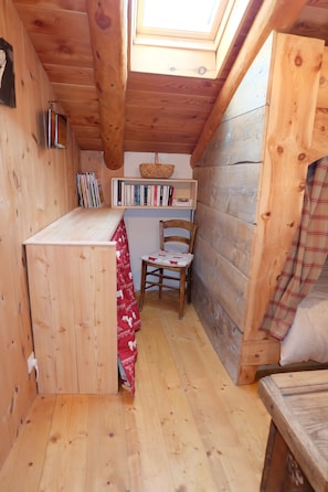 A cozy wooden cabin with a skylight, a small table with a red and white tablecloth, a chair, and a bookshelf filled with books.