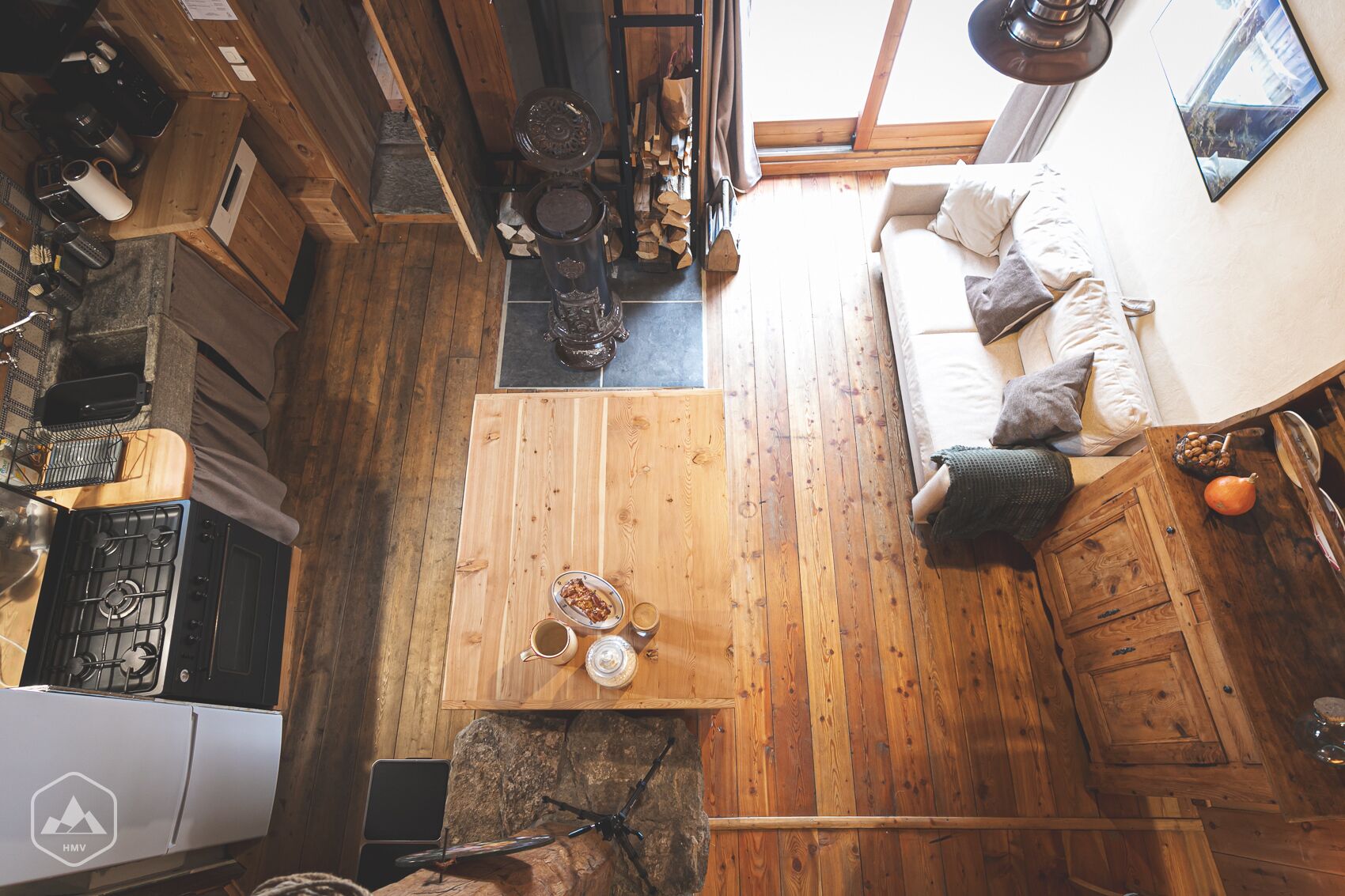 Une cabane chaleureuse avec une table à manger en bois, un canapé et un coin cuisine équipé d’une cuisinière et de divers ustensiles.