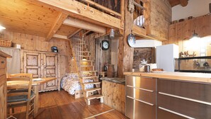 A rustic wooden interior with a wooden staircase, a bed, a kitchen area with stainless steel appliances, and wooden cabinets. - Le Chalet du Papote (Aussois)
