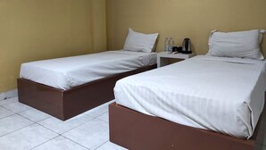 Quarto de hotel com duas camas de solteiro, uma mesinha com chaleira e uma tomada na parede.