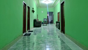 Um corredor com paredes verdes, uma luminária no teto, um sofá e uma televisão.