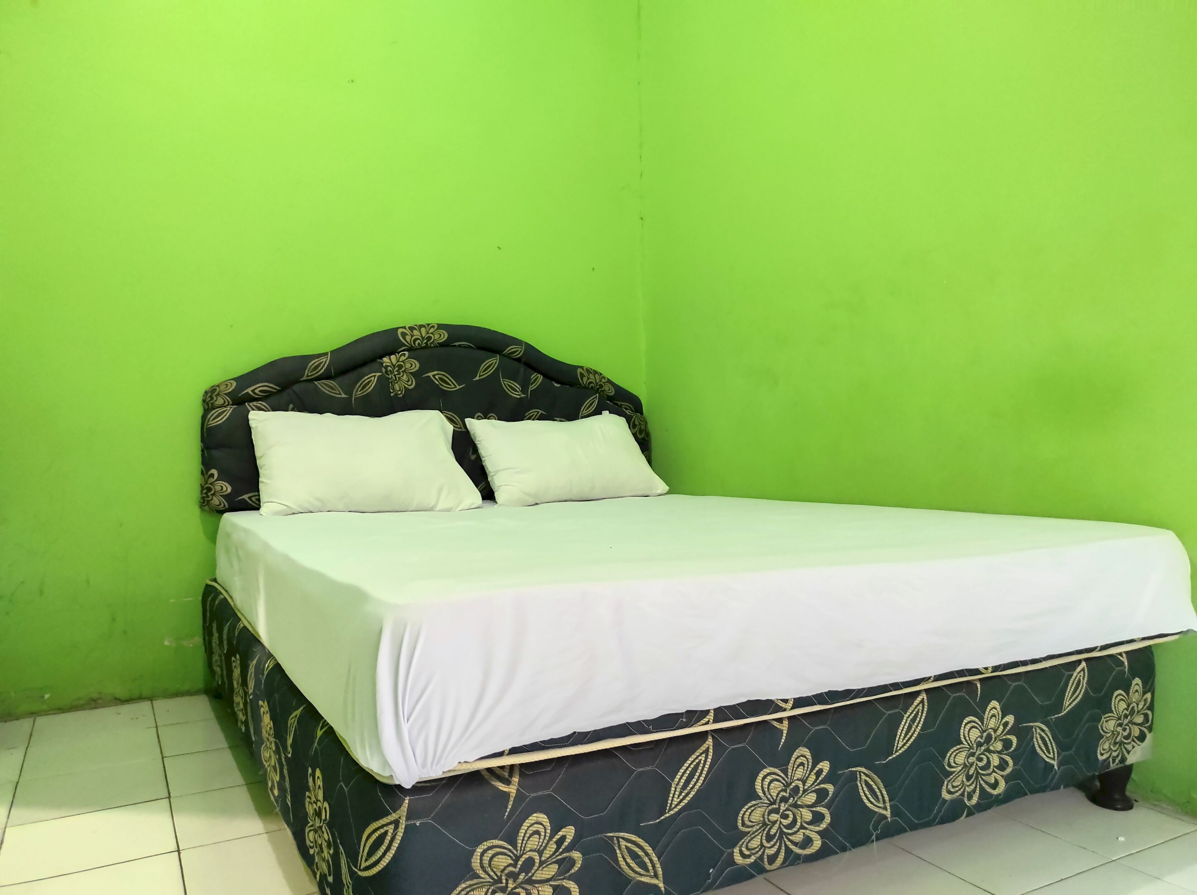 Een enkel bed met een bloemenprintdeken en een donker hoofdbord tegen een groene muur.
