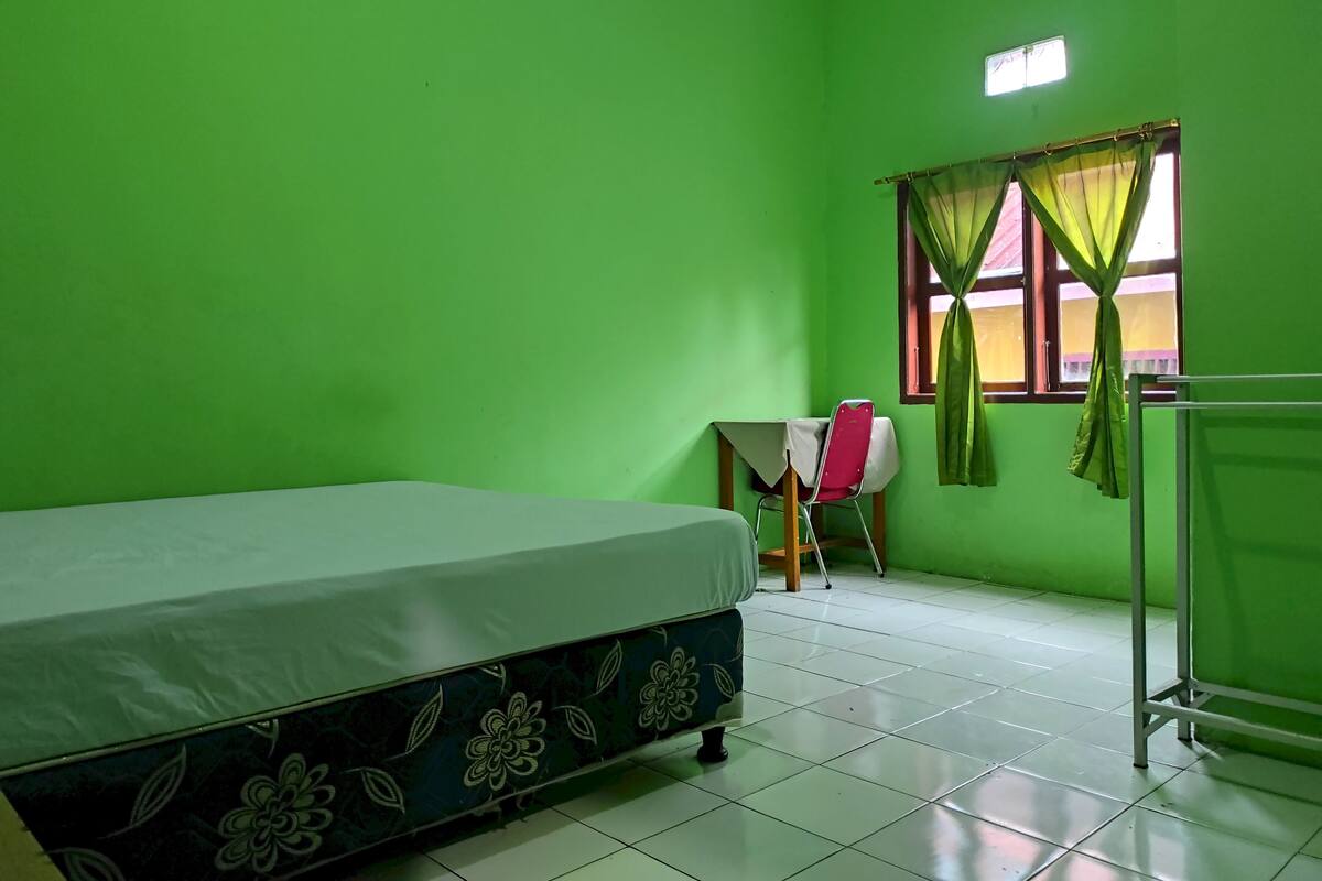 Una habitación con cama, una silla, una mesa y un ventanal con cortinas.
