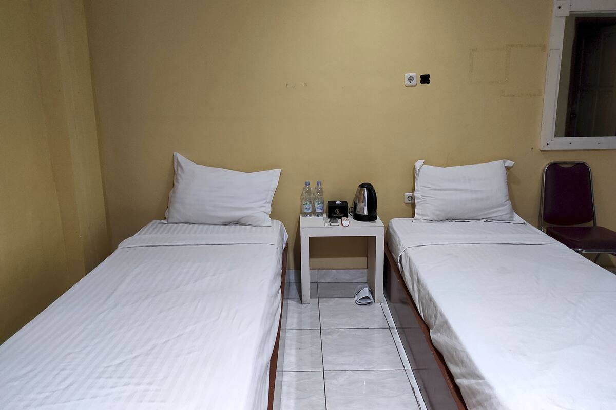 Habitación de hotel con dos camas individuales, una mesita de noche con hervidor de agua, botellas de agua y teléfono.