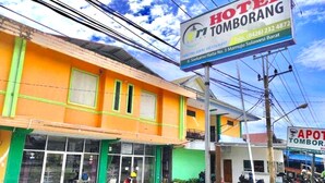 Um hotel com fachada laranja vibrante, uma placa com informações de contato e uma motocicleta estacionada na frente.