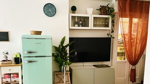Un espacio habitable compacto con un refrigerador verde azulado antiguo, un televisor de pantalla plana, una pequeña zona de comedor y una alfombra colorida.