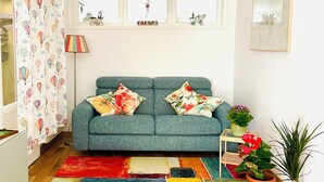 Una sala de estar con un sofá color turquesa, alfombras coloridas y plantas en macetas.