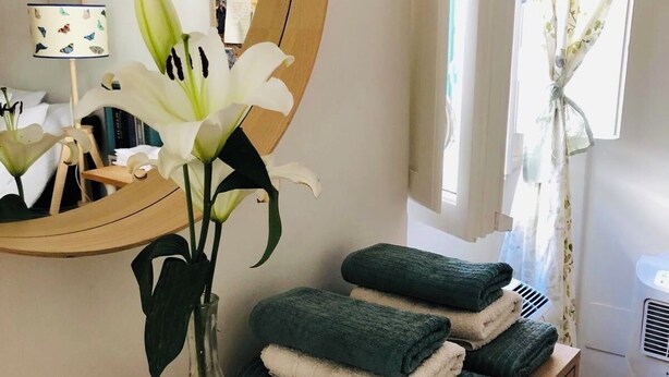 Un tocador de baño con espejo, un jarrón con lirios blancos y toallas dobladas.