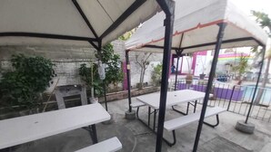 Un patio exterior con mesas de picnic blancas y una zona cubierta para sentarse.