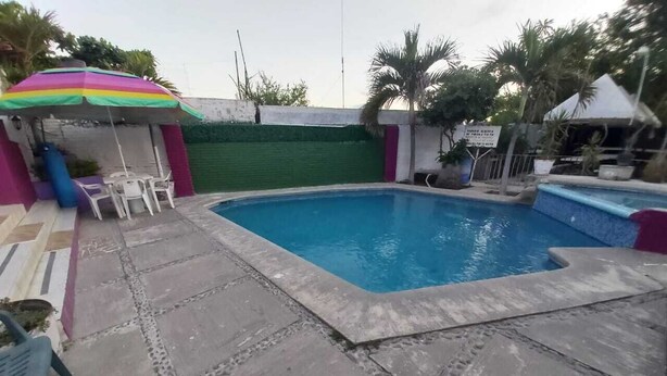 Una piscina con un borde de baldosas, una pequeña mesa con sillas y un paraguas colorido.