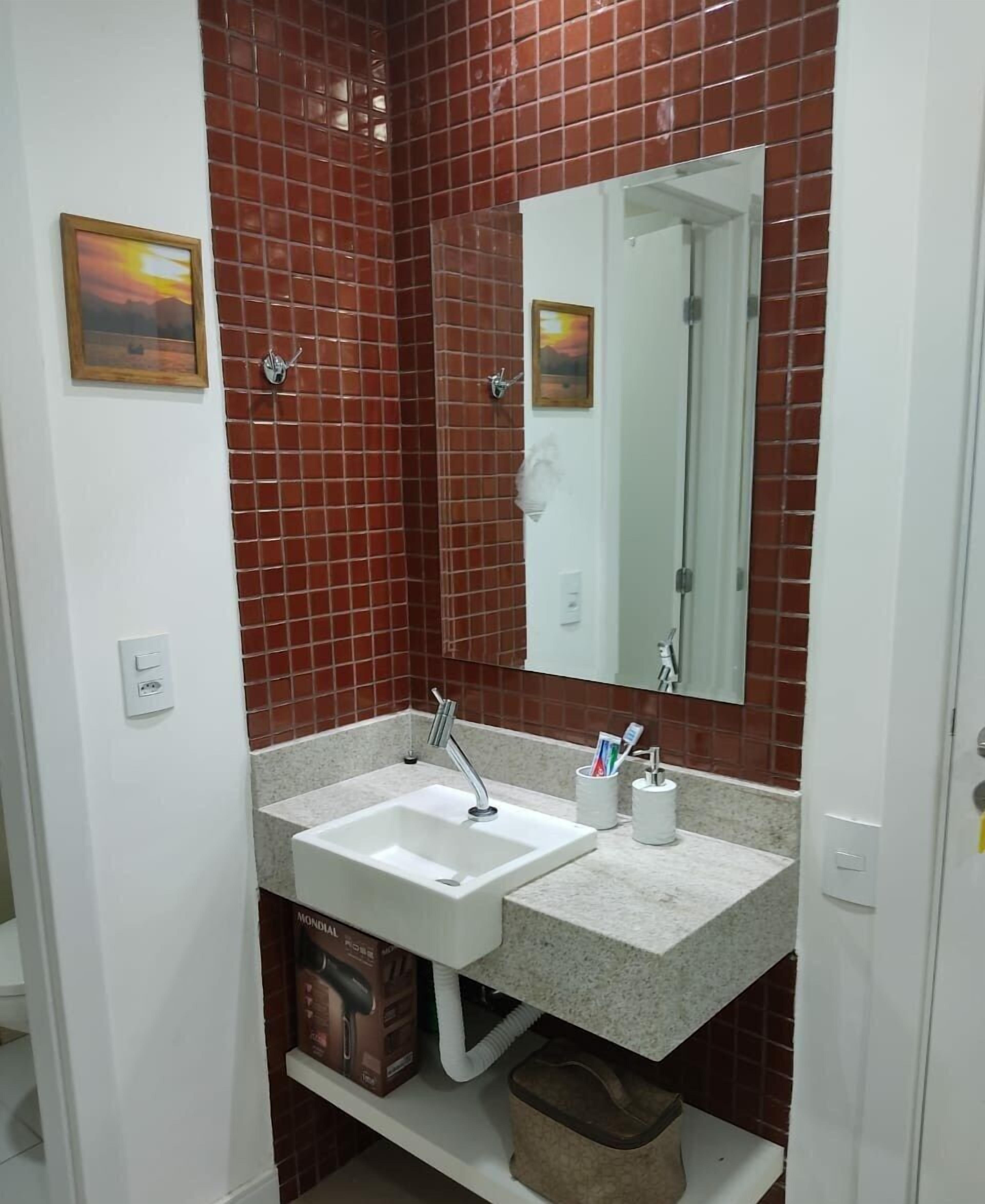A bathroom with red-tiled walls, a white sink, and a mirror.