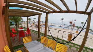 A covered outdoor seating area with a table and chairs, overlooking a beach.