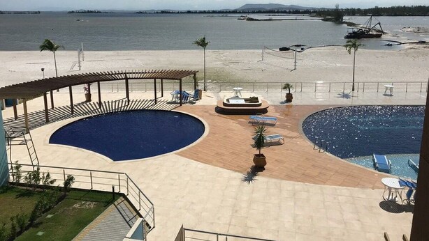 A pool area with two distinct sections, a covered seating area, and a view of the beach and water.