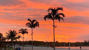 A beachside area with palm trees, chairs, and a view of the sunset over the water.
