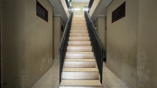 A long, narrow hallway with a central staircase, flanked by walls with ventilation grilles. - OYO 93412 Kost Irma Syariah Near UPTD SMP Negeri 8 Parepare (Parepare)