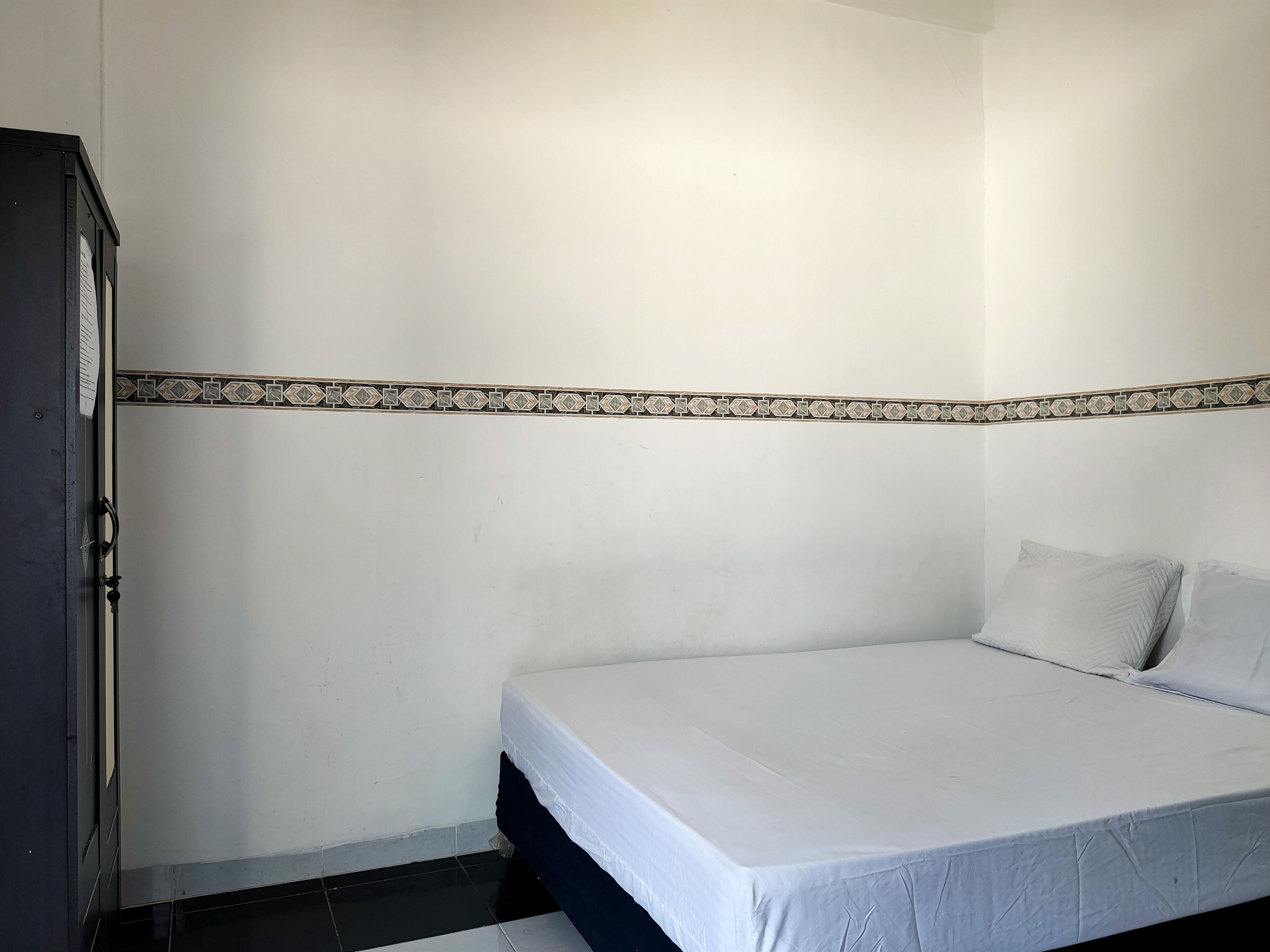 A small, clean room with a single bed, a wardrobe, and a decorative border on the wall.