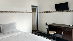 A small, simple room with a bed, a desk, a chair, a mirror, and a TV. - OYO 93412 Kost Irma Syariah Near UPTD SMP Negeri 8 Parepare (Parepare)