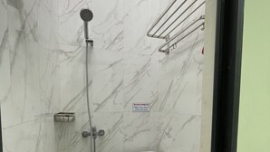 A bathroom with a toilet, a shower, and a green basket. - OYO 93412 Kost Irma Syariah Near UPTD SMP Negeri 8 Parepare (Parepare)