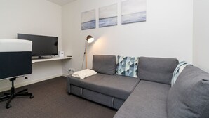 A modern room with a grey sofa, a desk with a computer, a flat-screen TV, and three abstract wall art pieces.