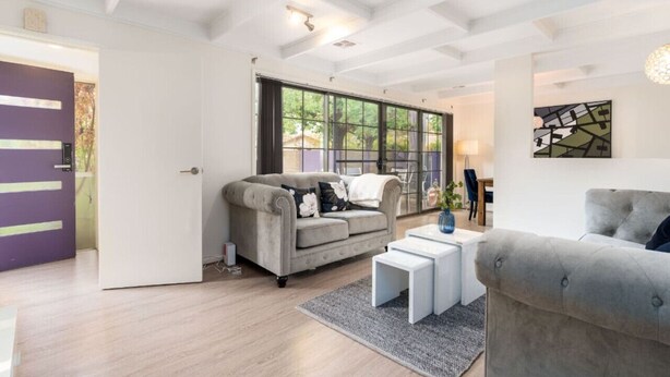 A modern living room with a grey sofa, a white coffee table, and a large window with a view of trees. - 4BR/2BA House Nestled in a Quiet Spot in Dickson (Dickson)