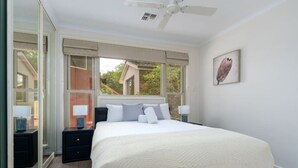 A bedroom with a large bed, two bedside tables, a ceiling fan, and a window with a view of a house. - 4BR/2BA House Nestled in a Quiet Spot in Dickson (Dickson)