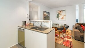 A compact kitchen with a dishwasher, a sink, and a dining area with a table and chairs. - 2BR Apartment near Parliament House (Barton)