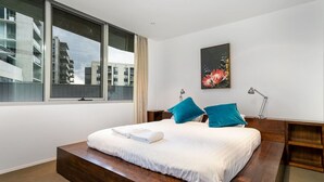 A modern bedroom with a large bed, a city view, and a painting on the wall. - 2BR Apartment near Parliament House (Barton)