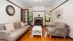 Een woonkamer met twee banken, een bijzettafeltje, een open haard en een klok aan de muur.