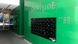 Un mur végétal orné du mot « QUAYSIDE » et d’une rangée de boîtes aux lettres noires, chacune portant le numéro de l’unité.