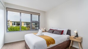 Une chambre d’hôtel moderne avec une grande fenêtre, un lit bien fait, une table de chevet avec une lampe et une vue sur l’extérieur.
