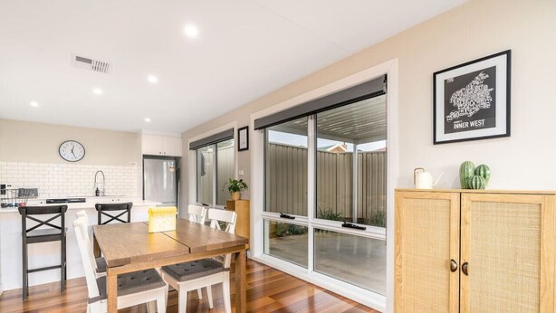A modern kitchen with white cabinets, a wooden dining table, and a large sliding glass door leading to a patio.