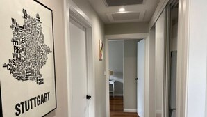 A hallway with a framed map of Stuttgart on the wall, leading to a room with a bed and a nightstand.