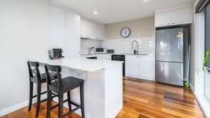 A modern kitchen with white cabinets, a stainless steel refrigerator, a microwave, and a clock on the wall.