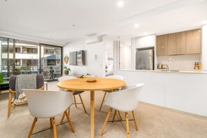 A modern kitchen with white cabinets, a stainless steel refrigerator, and a wooden dining table with white chairs.
