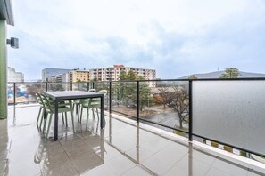 A balcony with a table and chairs, a glass railing, and a view of a building and trees. - Roomy 2BR/2BA City-Centre Apt (Braddon)