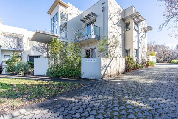 A modern two-story residential building with a paved driveway and a small garden area.