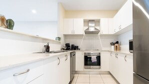 A modern kitchen with white cabinets, stainless steel appliances, and a tiled floor. - Captivating 3BR/2BA APT close to Dickson Shopping! (Lyneham)