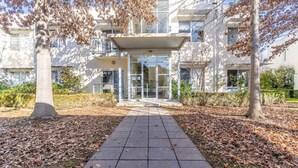 A modern building with a covered entrance, a paved walkway, and leaf-covered ground. - Captivating 3BR/2BA APT close to Dickson Shopping! (Lyneham)