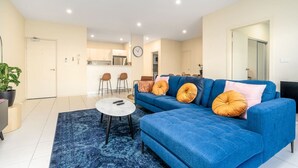 A modern living room with a blue sofa, a coffee table, and a blue rug. - Captivating 3BR/2BA APT close to Dickson Shopping! (Lyneham)
