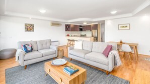 A modern living room with two grey sofas, a wooden coffee table, and a kitchen in the background. - 2BR/2BA Apt w/ Dedicated Workspace & Free parking! (Griffith)