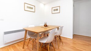A dining area with a wooden table and white chairs, framed pictures on the wall, and a radiator on the wall. - 2BR/2BA Apt w/ Dedicated Workspace & Free parking! (Griffith)