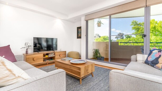 A modern living room with a sofa, coffee table, TV, and a sliding glass door leading to a balcony. - 2BR/2BA Apt w/ Dedicated Workspace & Free parking! (Griffith)