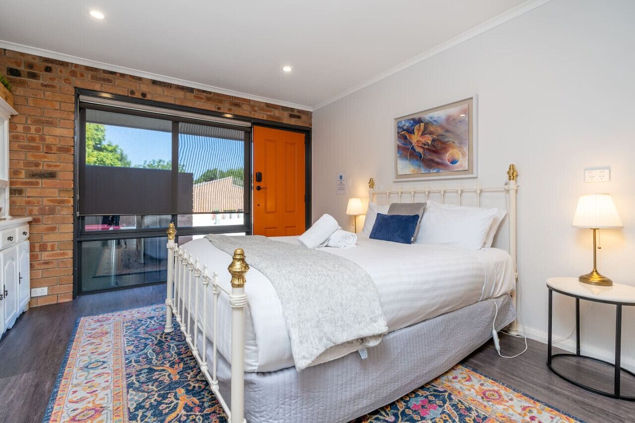 Een slaapkamer met een bed, nachtkastje, lamp, schilderij en een schuifpui naar een buitenruimte.