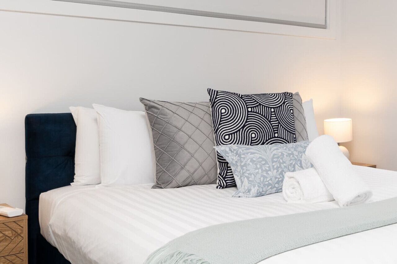 A neatly made bed with white linens, a dark blue headboard, and patterned pillows.