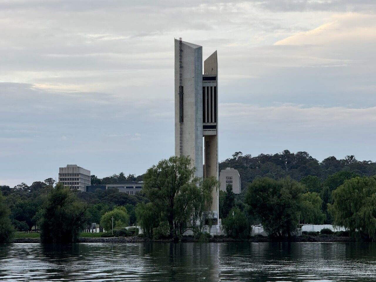Un edificio alto y moderno con un diseño arquitectónico distintivo, ubicado junto al agua, con árboles y otros edificios al fondo.
