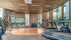 Une salle de sport spacieuse équipée de machines de cardio, de postes d’entraînement avec poids et d’un mur recouvert de miroirs.