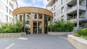Un bâtiment moderne doté d’une entrée incurvée, de grandes fenêtres et d’une cour dallée agrémentée de verdure.