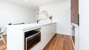 Une cuisine moderne avec des meubles blancs, un four encastré, un miroir rond et un plancher en bois.