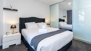 Et moderne hotelværelse med en stor seng, sengeborde, et spejl og en skydedør.