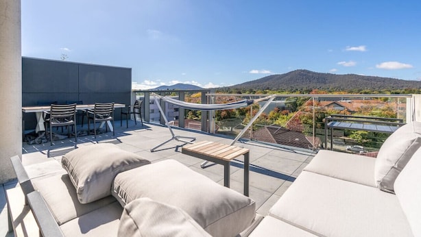 Una terraza en la azotea con mobiliario exterior, una hamaca y vistas a la montaña y al paisaje urbano.